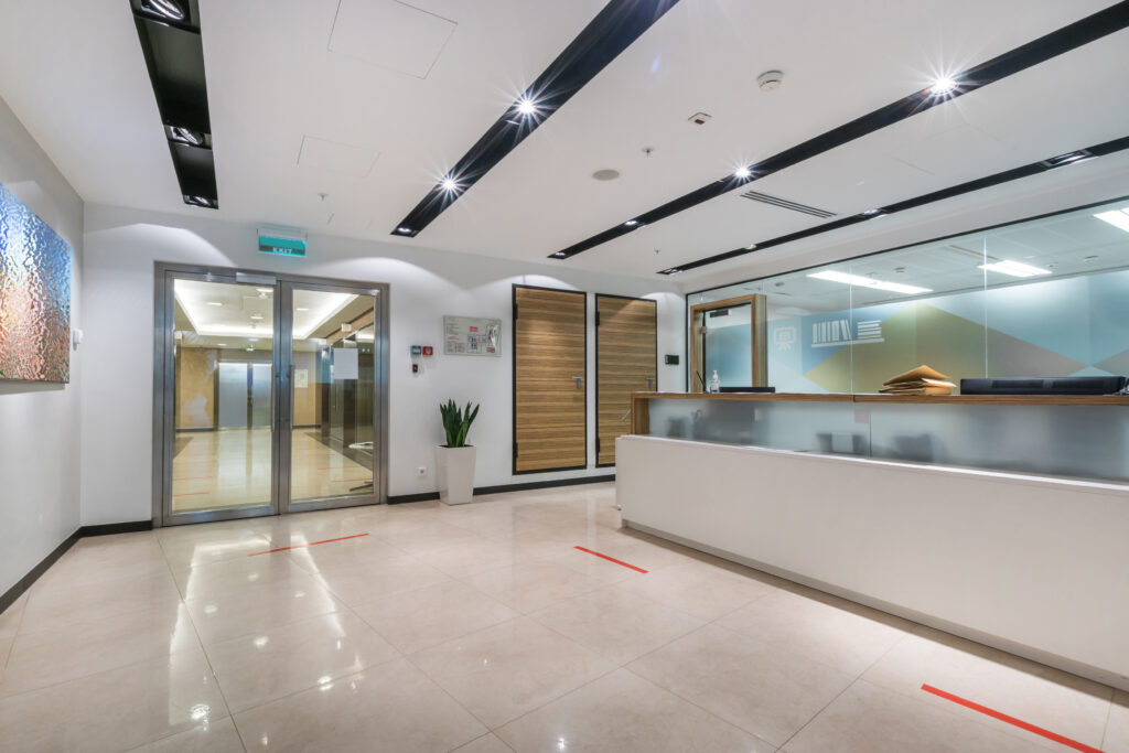 A spacious, bright office hall with a reception desk, glass doors and a picture on the wall.