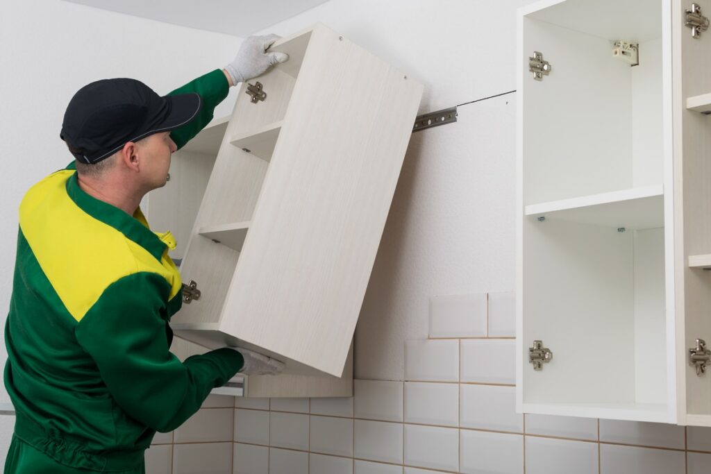 a worker hangs a kitchen cabinet on the wall Worker installing a cabinet door in a kitchen