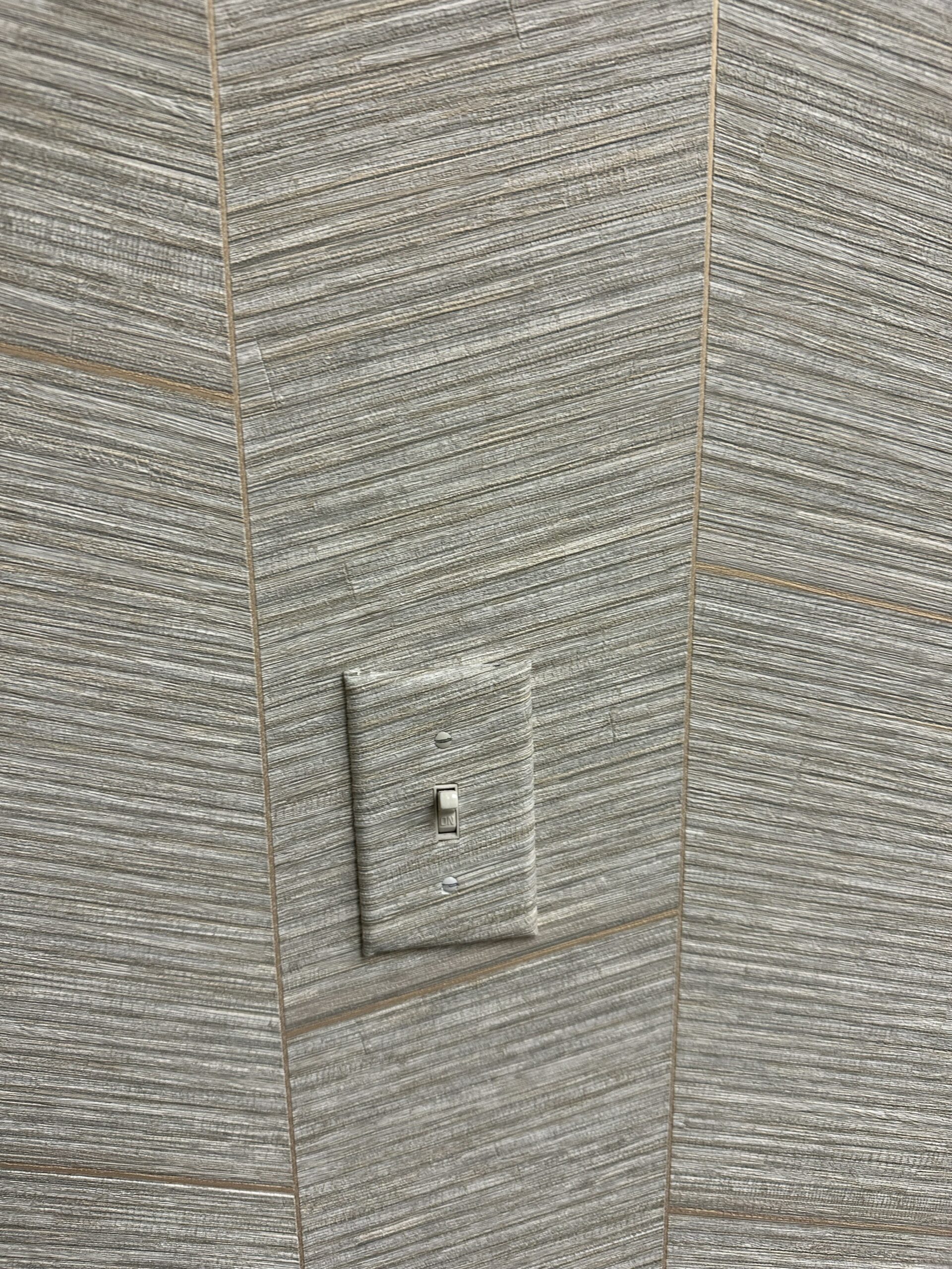 Seamless Wallpaper Installation Around Office Light Switches Close up of a light switch plate seamlessly covered with textured gray and beige wallpaper in an office.