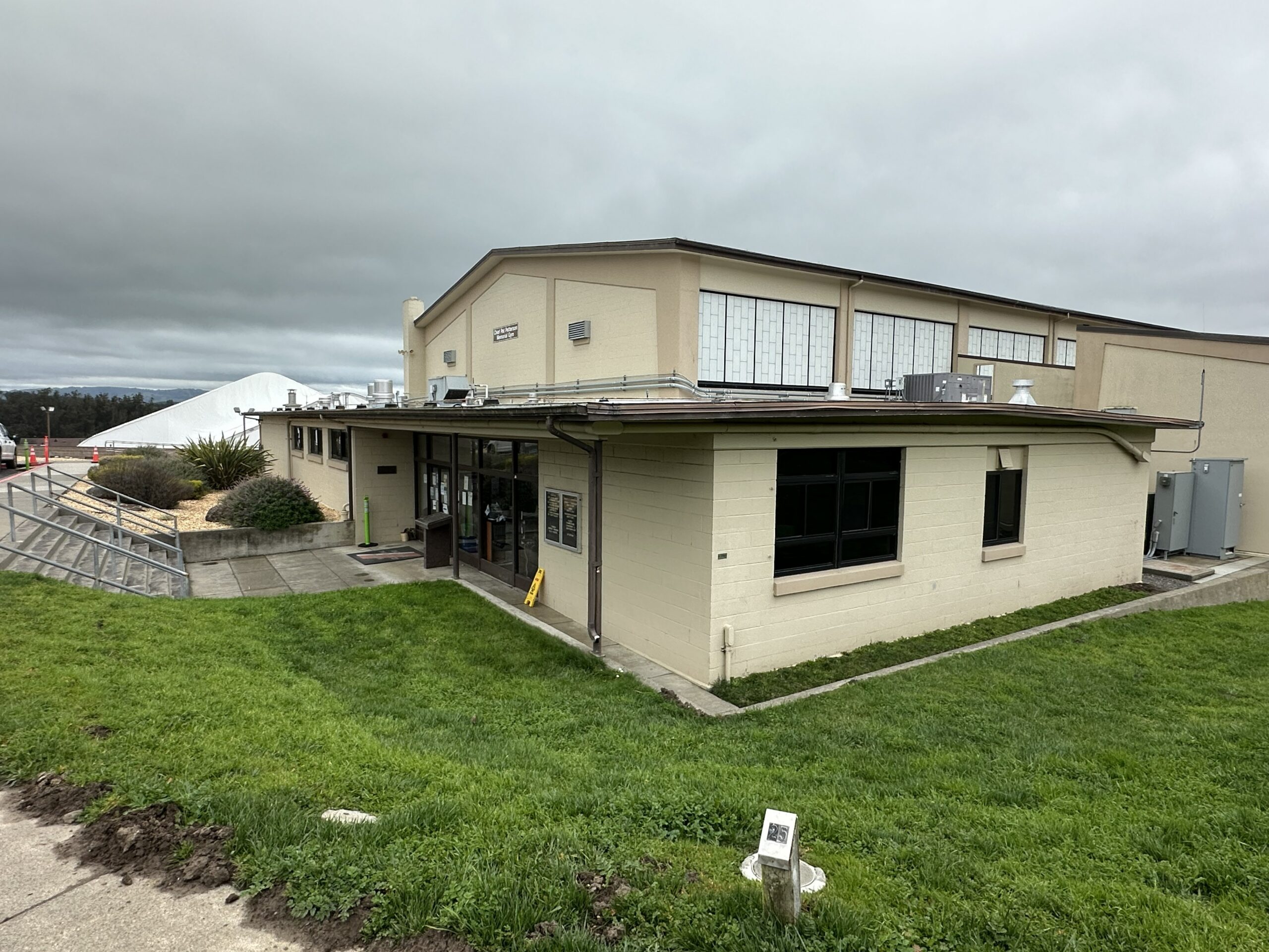 Commercial building exterior painting services The exterior of a large commercial building with light beige walls and dark windows under a cloudy sky.