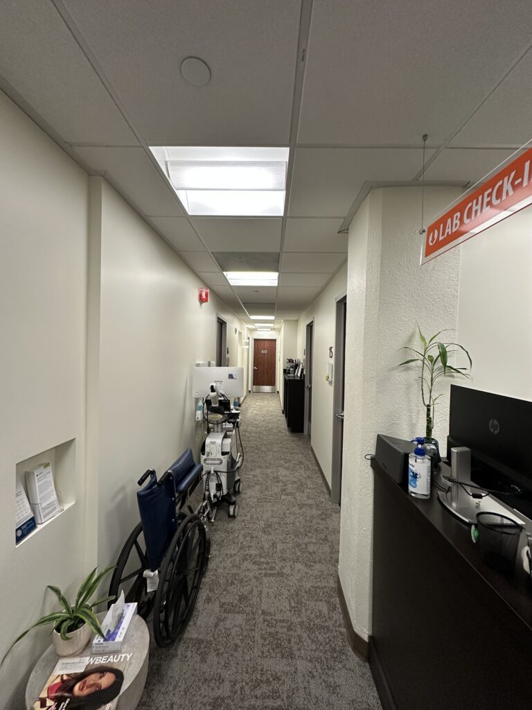 Cream-painted commercial interior hallway with suspended ceiling, fluorescent lighting, gray carpeted flooring, and office