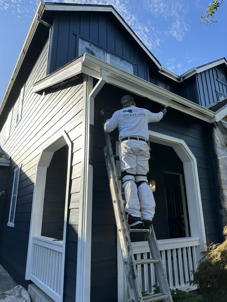Painter applying exterior paint to trim on a dark blue home